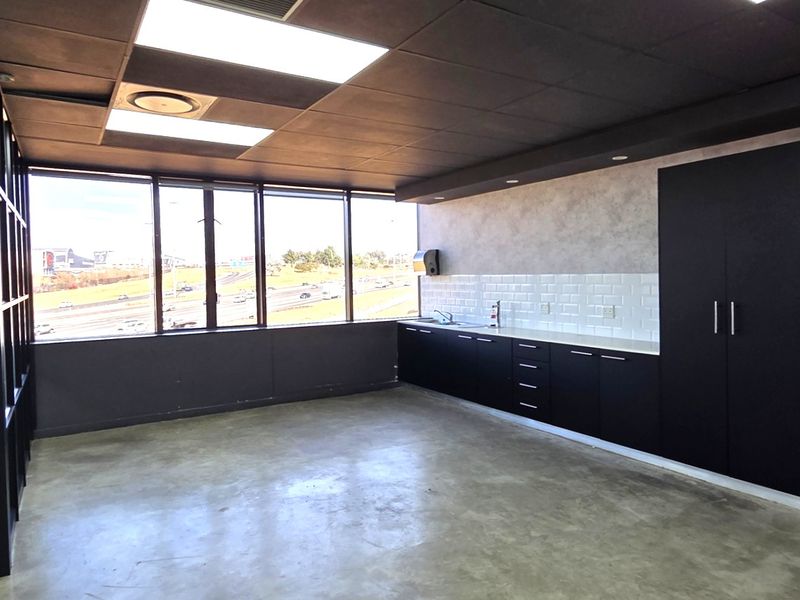 Modern office space featuring polished concrete floors, built-in kitchenette cabinetry with subway tile backsplash, and large windows with expansive views.