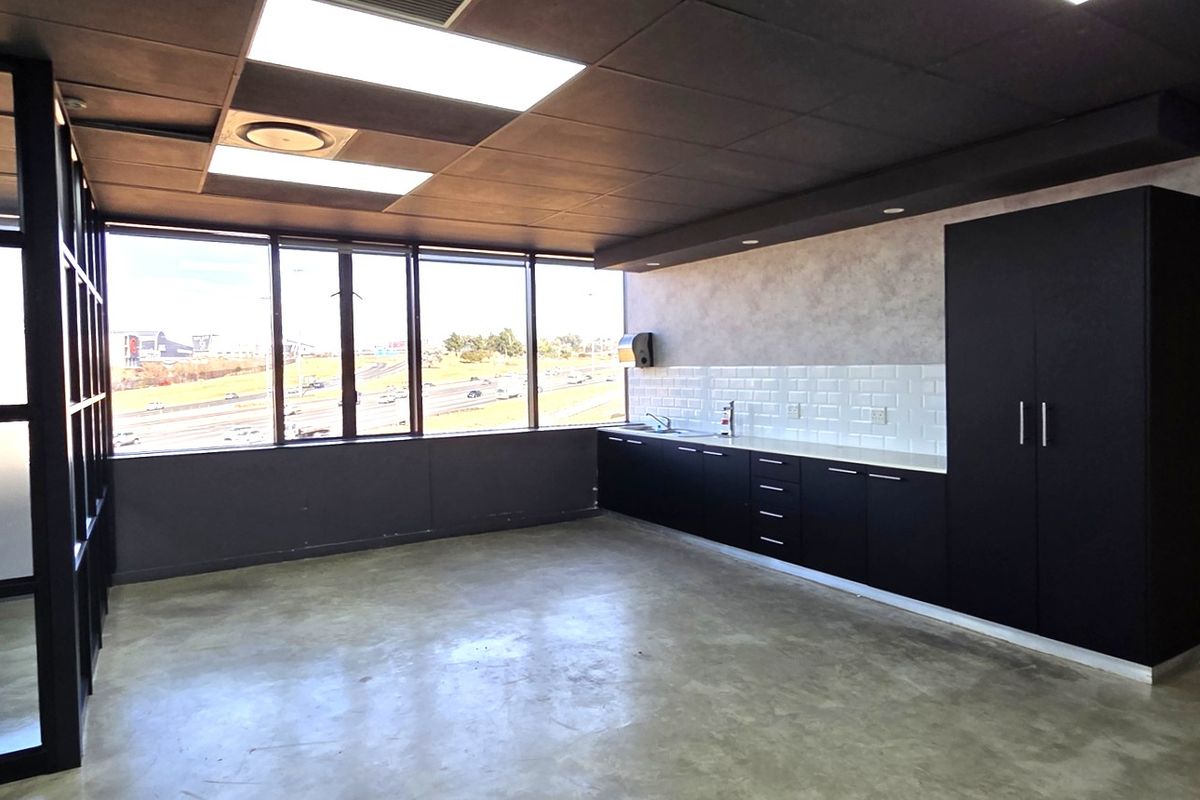Modern office space featuring polished concrete floors, built-in kitchenette cabinetry with subway tile backsplash, and large windows with expansive views.