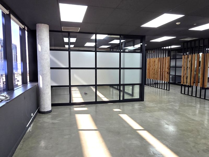 Modern open-plan office space featuring polished concrete floors, contemporary timber slat dividers, frosted glass partitions, and abundant natural light from large windows.