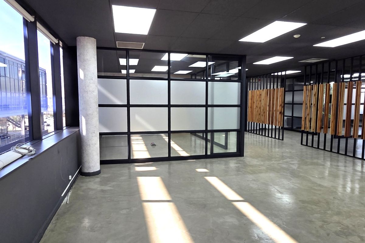 Modern open-plan office space featuring polished concrete floors, contemporary timber slat dividers, frosted glass partitions, and abundant natural light from large windows.