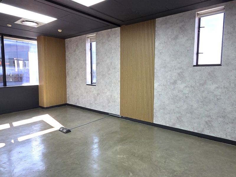 A modern, empty office space featuring polished concrete floors, timber slat wall accents, and large windows providing ample natural light.