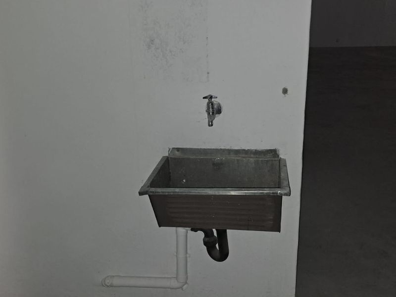 A basic utility sink with a wall-mounted tap, featuring exposed plumbing and a utilitarian finish.