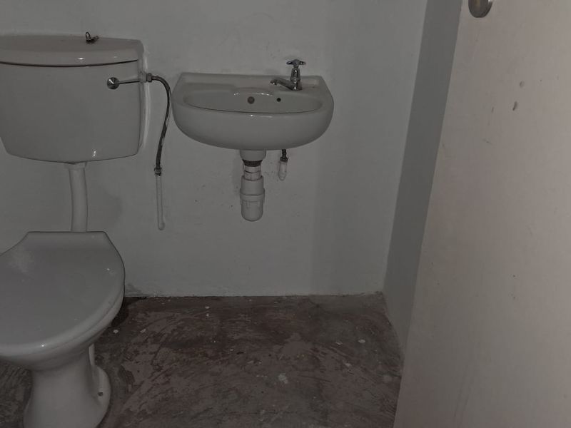 A compact, functional restroom featuring a wall-mounted basin and a standard toilet, currently in a basic, unfinished state.