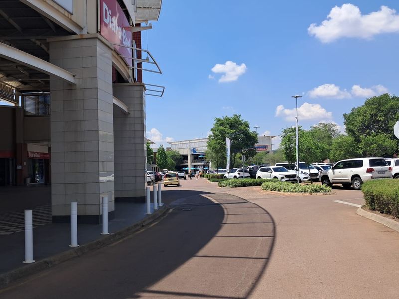Exterior view of a retail shopping center entrance with paved driveway, parking area, and modern building facade.