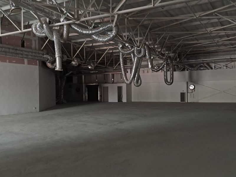 A large, open-plan retail space featuring high ceilings with exposed industrial ductwork and concrete flooring, suitable for a variety of commercial uses.