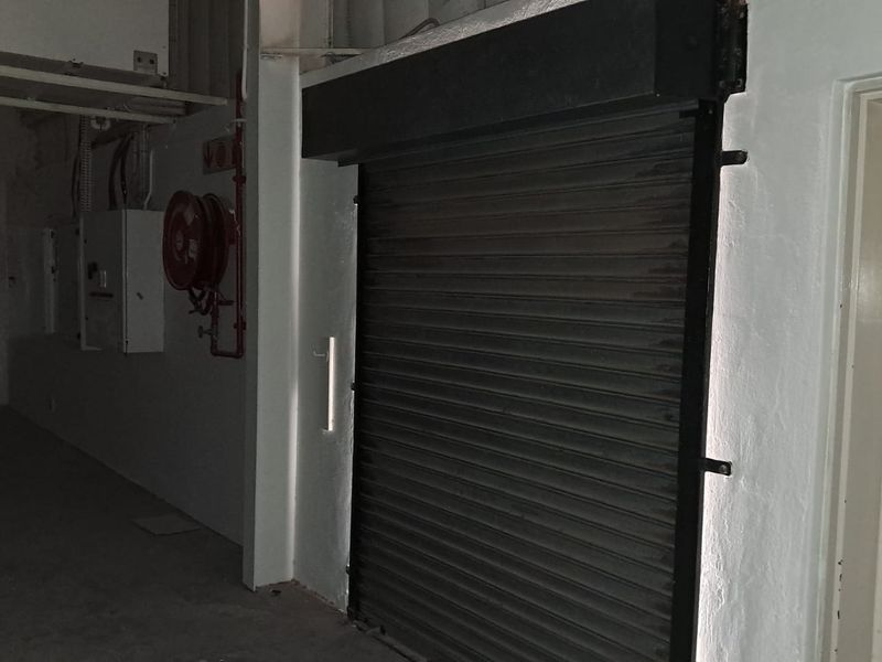 Interior utility space featuring a secure metal roller shutter door, fire hose reel, and exposed electrical distribution boards.