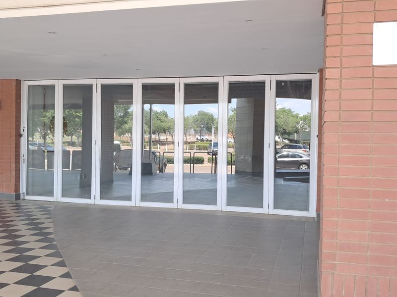 A retail storefront entrance featuring large glass folding doors, brick facade detailing, and tiled flooring under a covered walkway.