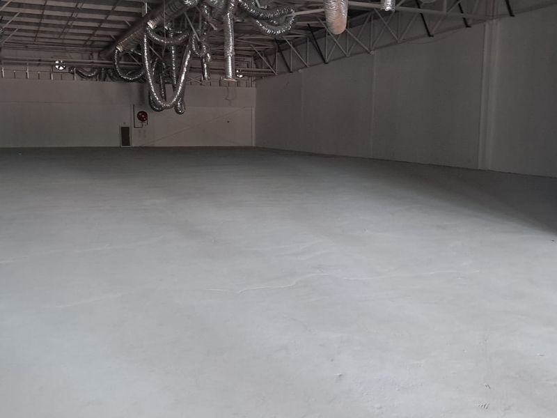 A spacious, open-plan retail or industrial unit featuring exposed ceiling ductwork, painted walls, and a concrete floor.