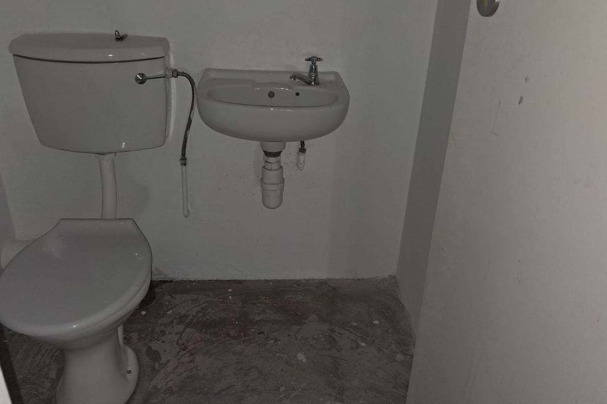 A compact, functional restroom featuring a wall-mounted basin and a standard toilet, currently in a basic, unfinished state.