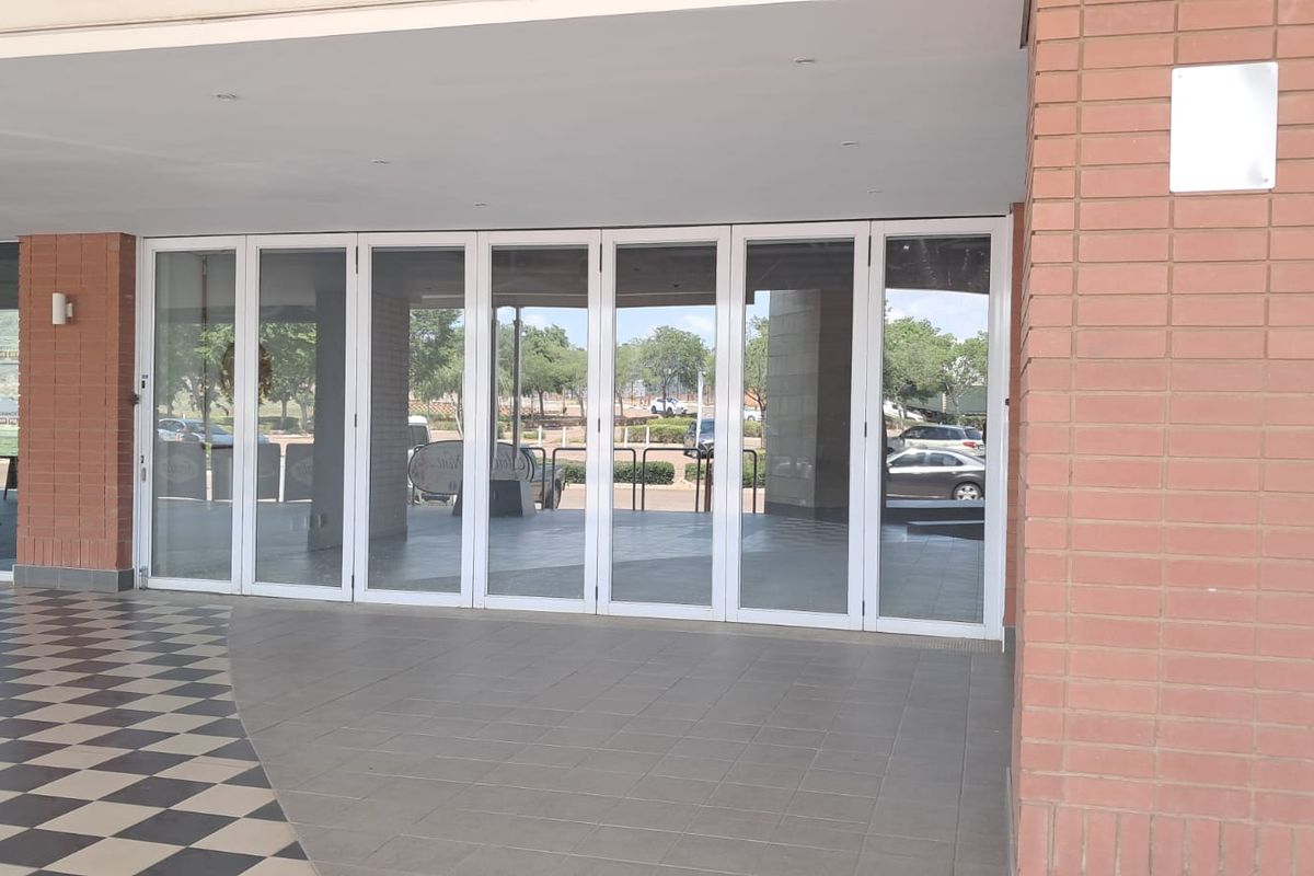 A retail storefront entrance featuring large glass folding doors, brick facade detailing, and tiled flooring under a covered walkway.