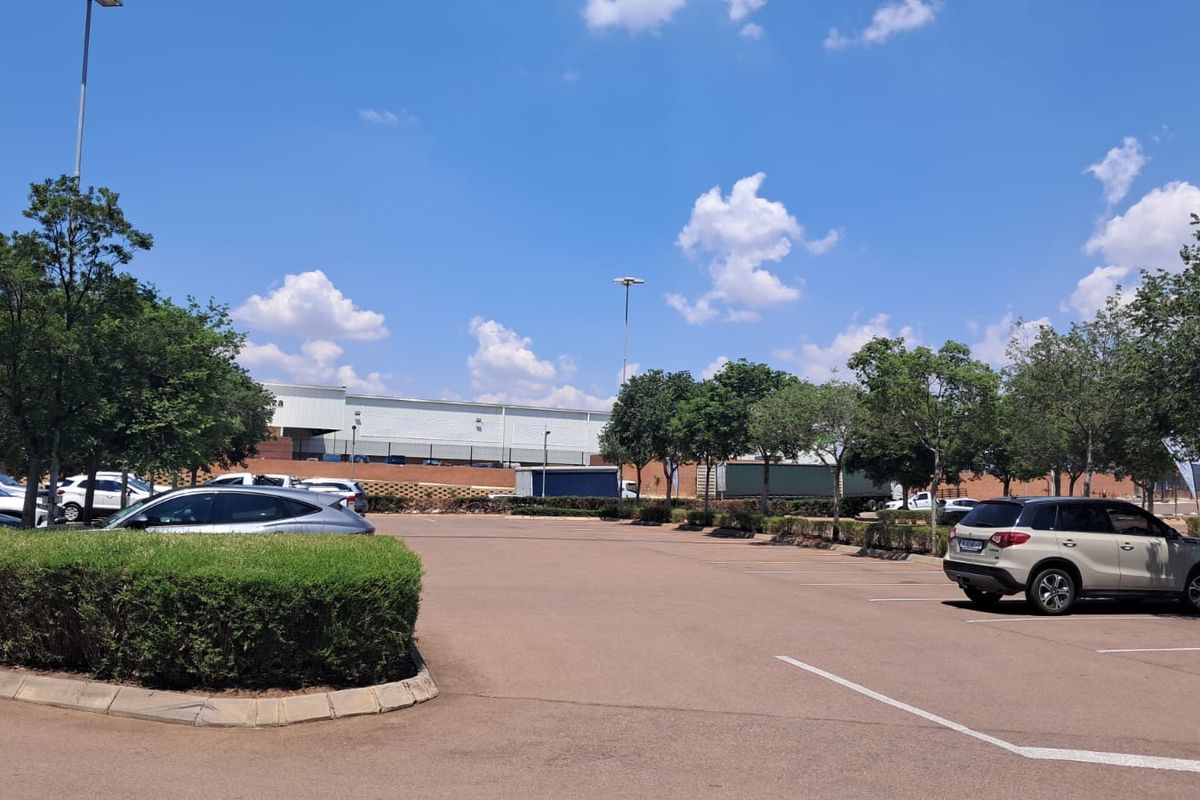 A view of the paved parking area and landscaped garden beds at the retail property, featuring mature trees and clear access.