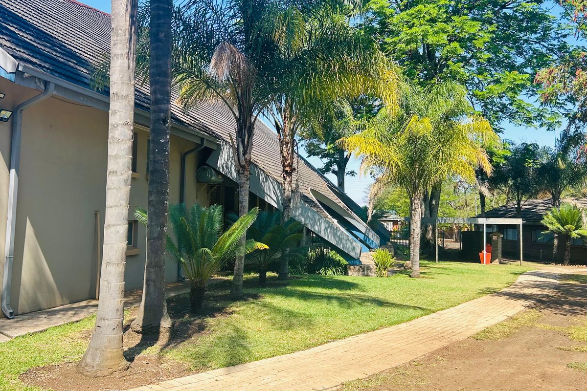 Rear exterior view of the commercial property featuring a paved walkway, landscaped garden areas, and tiled roof structure.