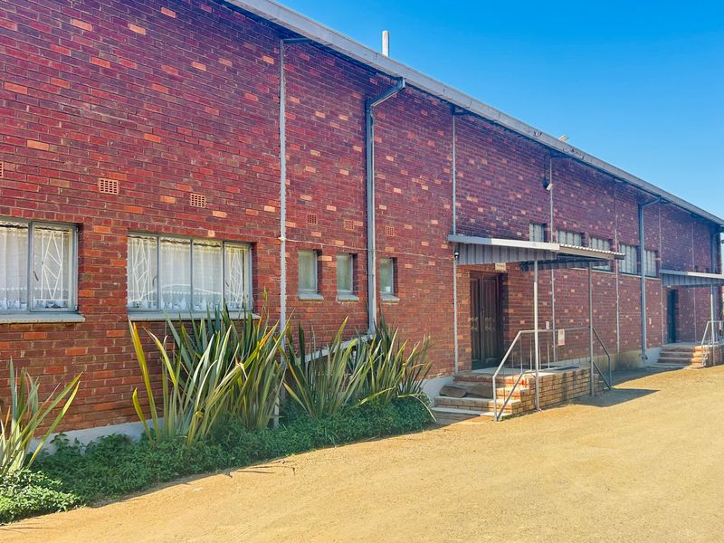 Exterior view of a commercial brick building featuring metal window frames, security bars, and covered entrance access points.
