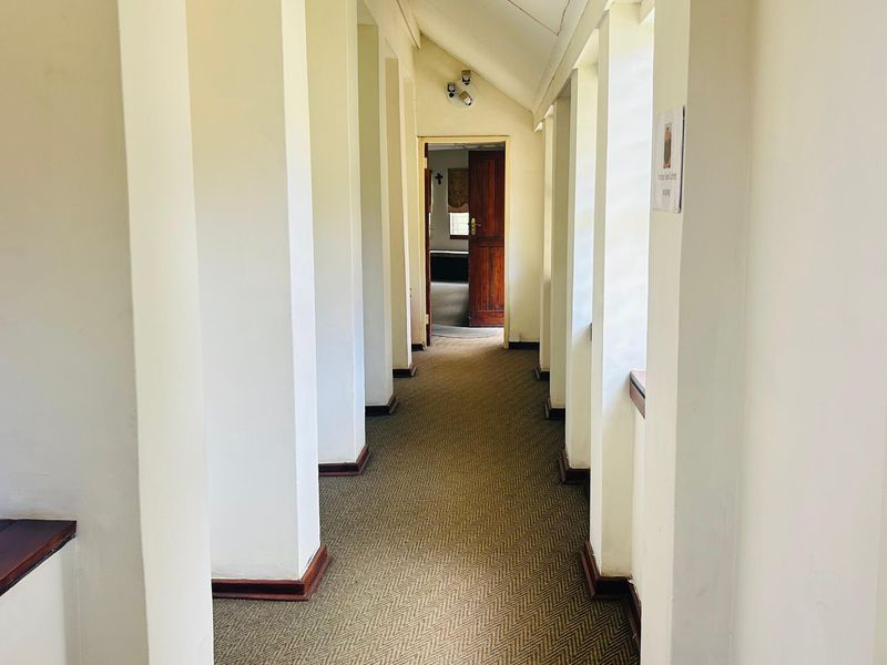 A long, carpeted hallway featuring a vaulted ceiling, timber skirting boards, and access to an adjoining room through a wooden door.
