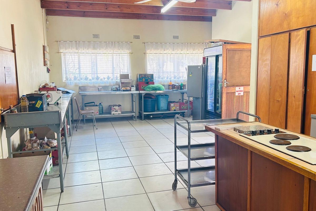 A functional commercial kitchen space featuring exposed timber ceiling beams, ceramic tiled flooring, built-in wooden cabinetry, and stainless steel preparation surfaces.