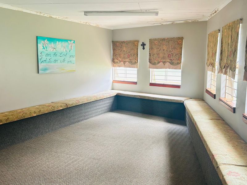 A commercial space featuring built-in perimeter bench seating, security bars on windows, and carpeted flooring, showing signs of ceiling water damage.
