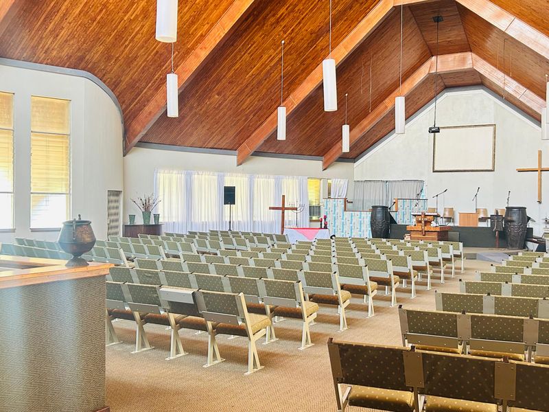 A spacious commercial hall featuring a high vaulted timber ceiling, carpeted flooring, and a raised stage area suitable for assembly or event use.