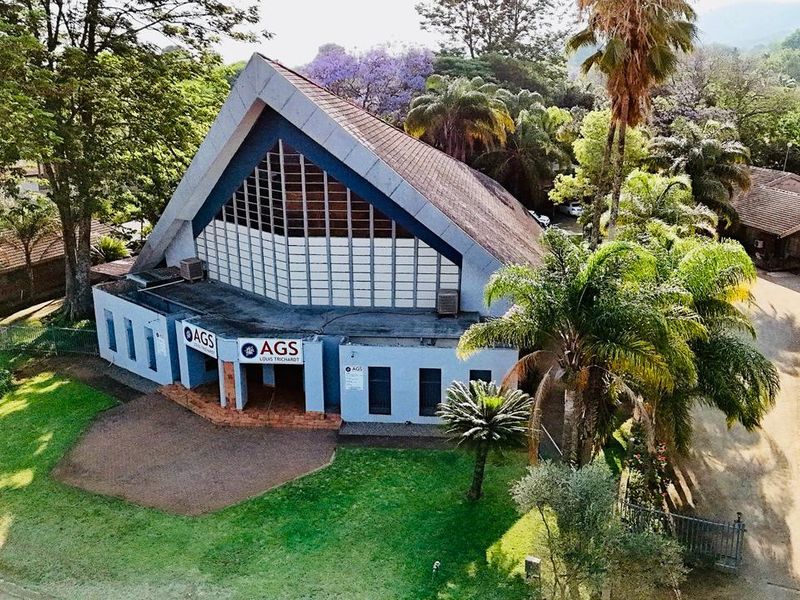 Aerial view of a commercial property featuring a distinctive pitched roof design, large glass facade, and surrounding landscaped grounds.