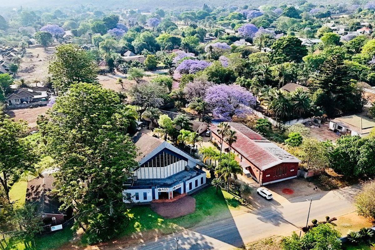 Aerial view of a commercial property complex featuring multiple buildings, mature trees, and paved access within a lush, green suburban setting.