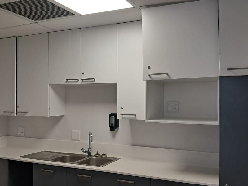 A functional office kitchenette featuring white cabinetry, a stainless steel double sink, and integrated counter space.