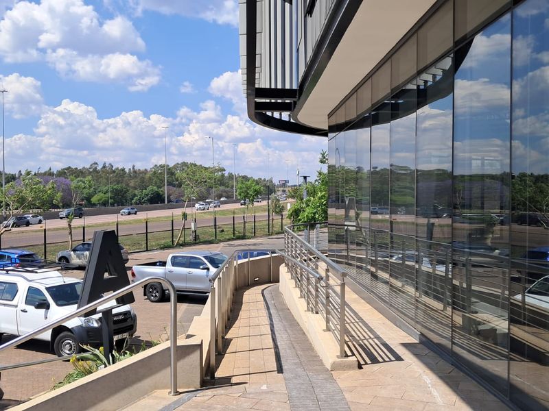 Modern office building exterior featuring a paved accessibility ramp with stainless steel railings and extensive glass curtain wall facade.