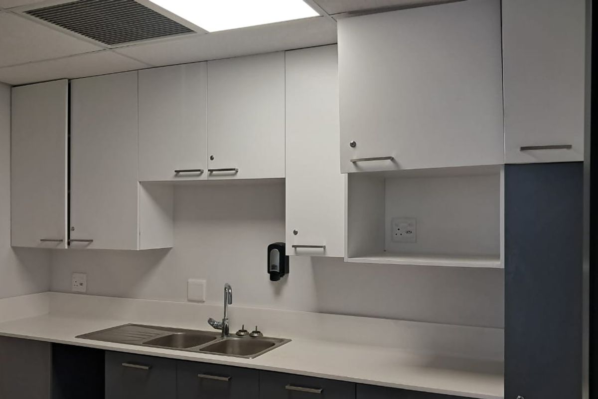 A functional office kitchenette featuring white cabinetry, a stainless steel double sink, and integrated counter space.