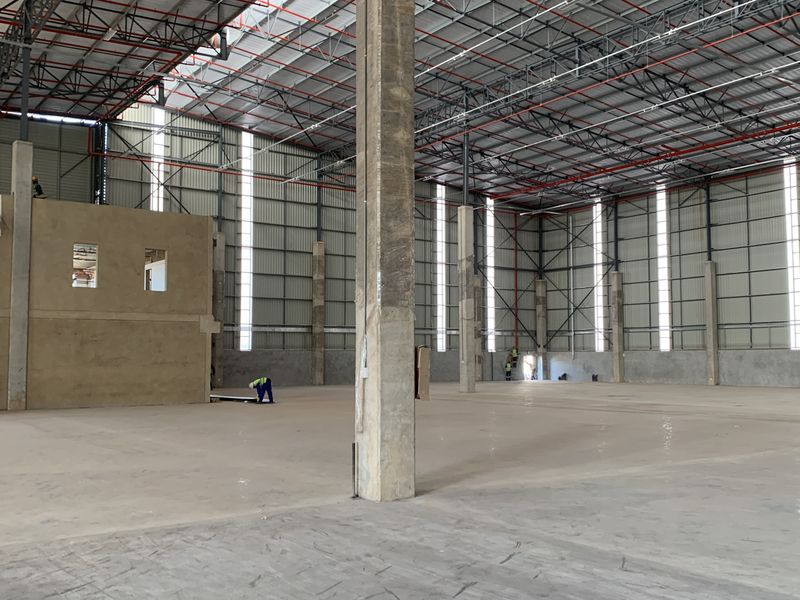 Large industrial warehouse space featuring high ceilings, exposed steel trusses, concrete flooring, and a mezzanine structure under construction.