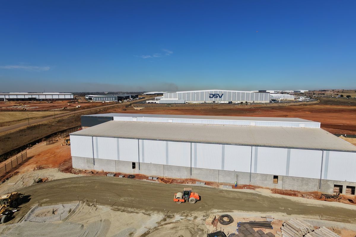 Aerial view of a large industrial warehouse facility under construction, featuring metal cladding and surrounding site development in an industrial park setting.