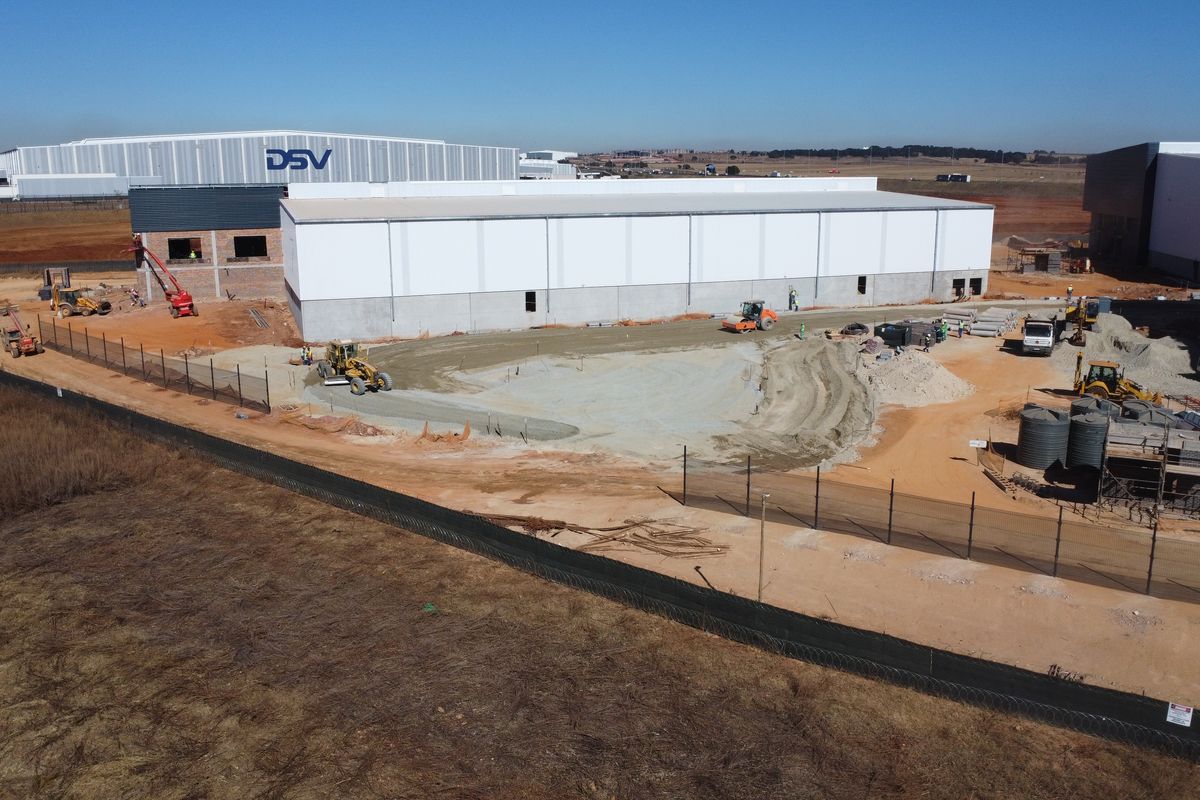 Aerial view of an industrial warehouse development site showing ongoing construction, site preparation, and perimeter fencing.