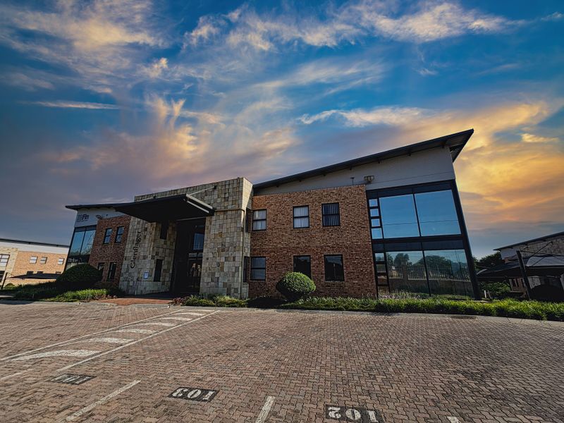 Professional exterior view of a modern office building featuring a brick and stone facade, large glass windows, and a paved parking area.