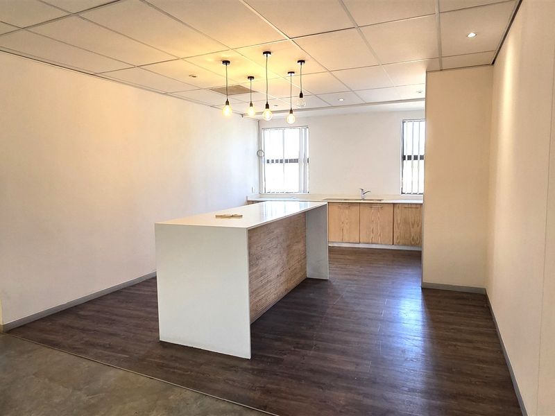 A clean, modern office kitchenette featuring a central island, built-in cabinetry with a sink, and a suspended ceiling with integrated lighting.