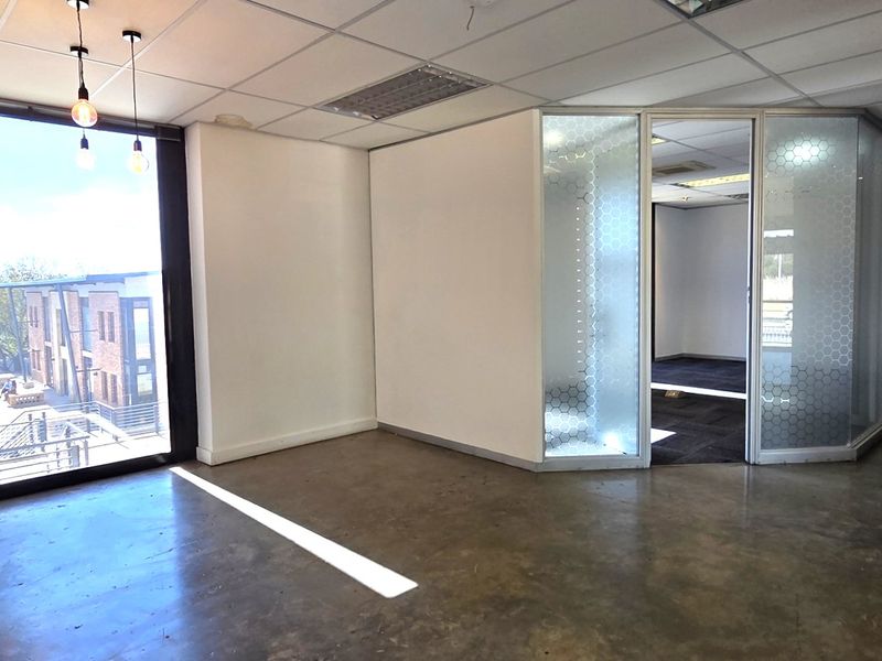 Modern open-plan office space featuring polished concrete floors, a suspended ceiling, and a glass-partitioned private office area with natural light.