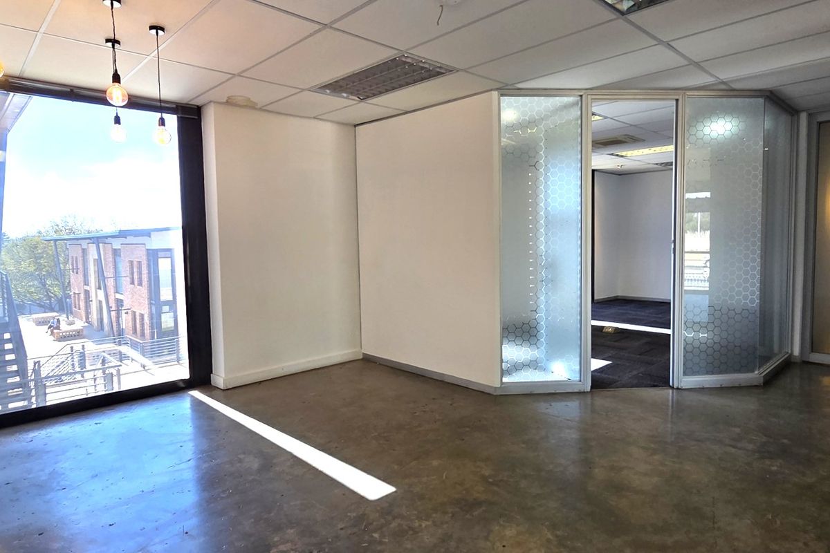 Modern open-plan office space featuring polished concrete floors, a suspended ceiling, and a glass-partitioned private office area with natural light.