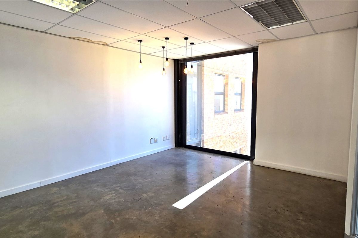 A bright, empty office space featuring polished concrete flooring, a suspended ceiling, and a large window providing natural light and exterior views.