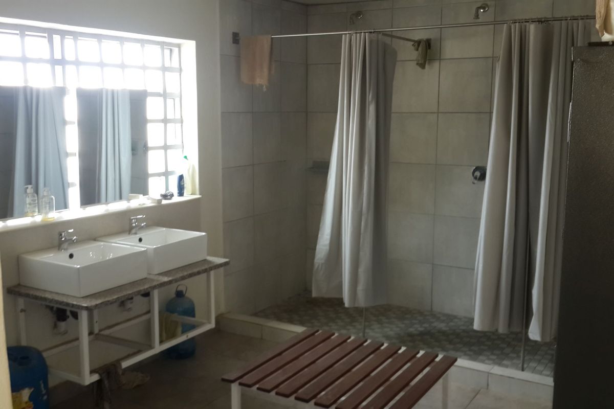 Functional industrial-style bathroom featuring a double vanity, walk-in shower area with tiled finishes, and a large glass block window for natural light.