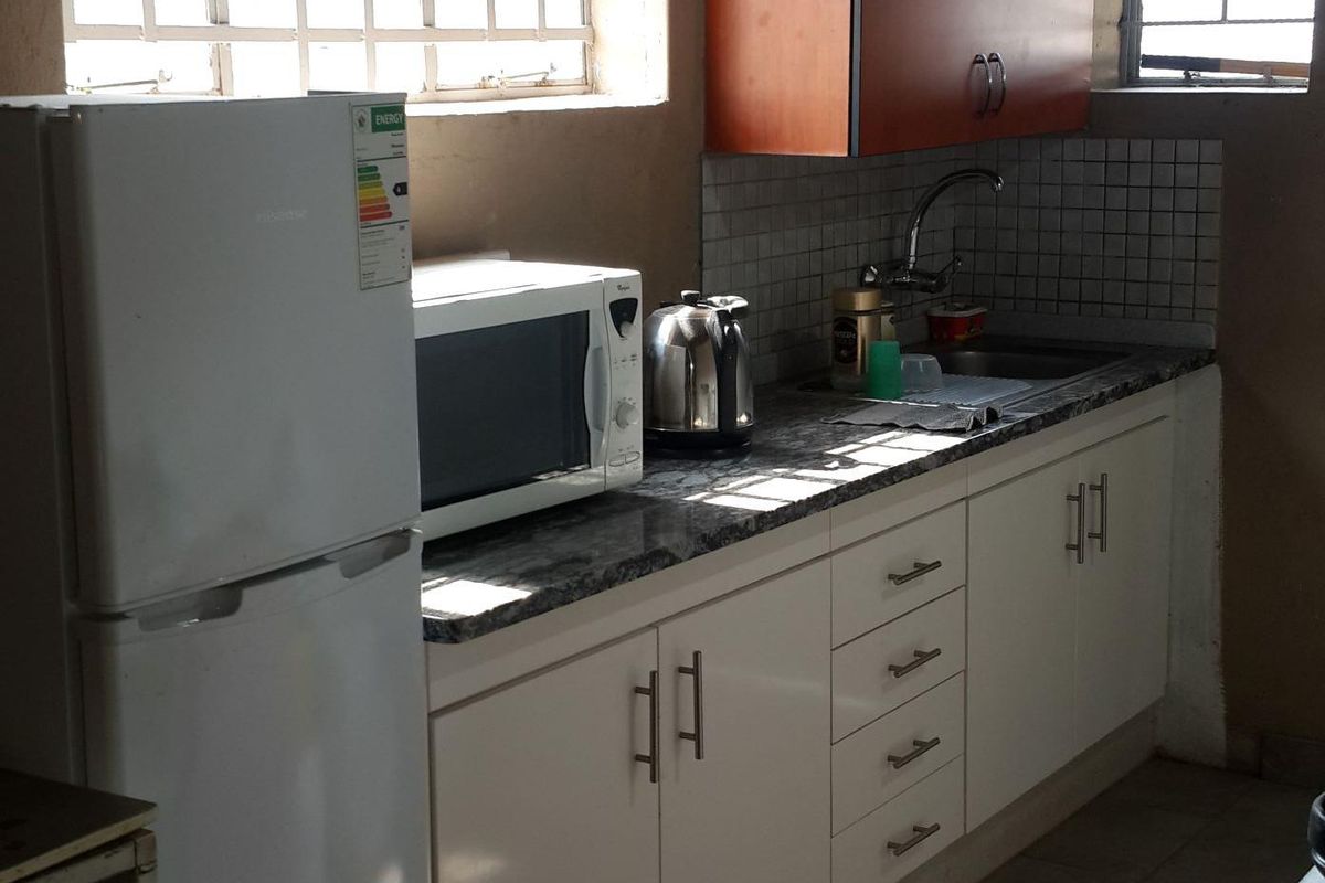 Compact industrial kitchen featuring granite countertops, white base cabinetry, orange wall-mounted cupboards, tiled backsplash, and security-barred windows.
