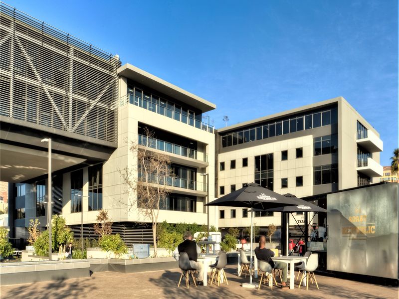 A modern multi-story office building featuring a contemporary glass and concrete facade with integrated sun shading and a spacious paved outdoor courtyard area.