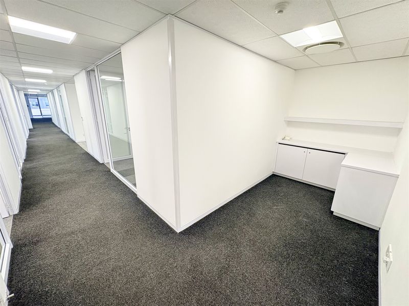 A clean, vacant office space featuring neutral carpet flooring, built-in storage cabinetry, and a glass partition wall, providing a professional and bright work environment.