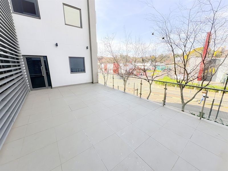 A spacious, modern balcony featuring tiled flooring and a sleek glass balustrade, offering an elevated view of the surrounding area.