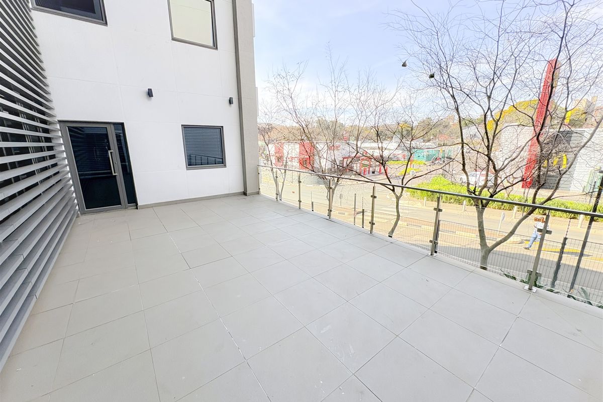 A spacious, modern balcony featuring tiled flooring and a sleek glass balustrade, offering an elevated view of the surrounding area.
