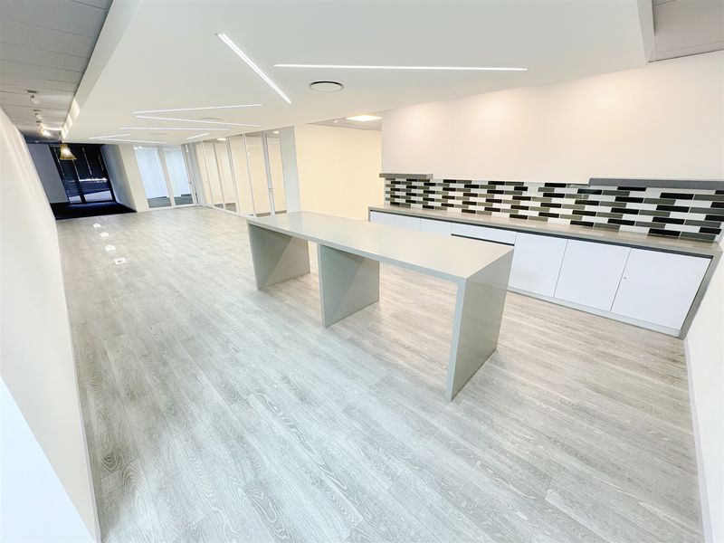 Modern open-plan office space featuring sleek built-in cabinetry, a central stone workstation, glass partitions, and contemporary recessed linear lighting.