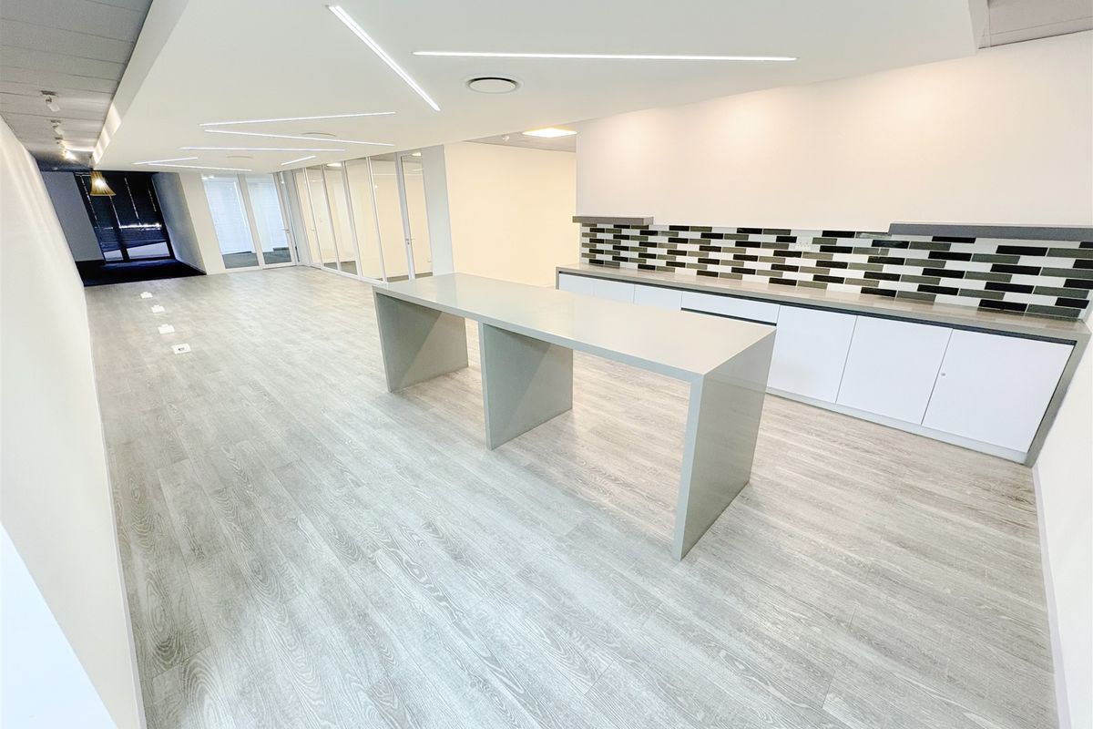 Modern open-plan office space featuring sleek built-in cabinetry, a central stone workstation, glass partitions, and contemporary recessed linear lighting.