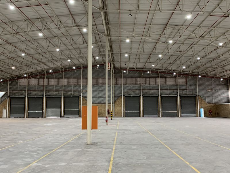 Spacious industrial warehouse featuring high ceilings, multiple roller shutter doors, concrete flooring, and an integrated fire sprinkler system.