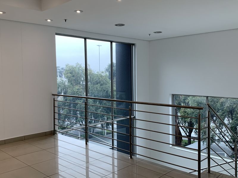 A bright, modern industrial hallway featuring polished floor tiles, a sleek stainless steel balustrade, and expansive windows providing ample natural light.