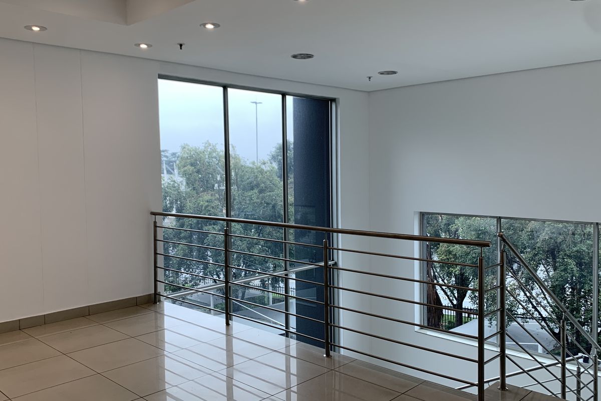 A bright, modern industrial hallway featuring polished floor tiles, a sleek stainless steel balustrade, and expansive windows providing ample natural light.
