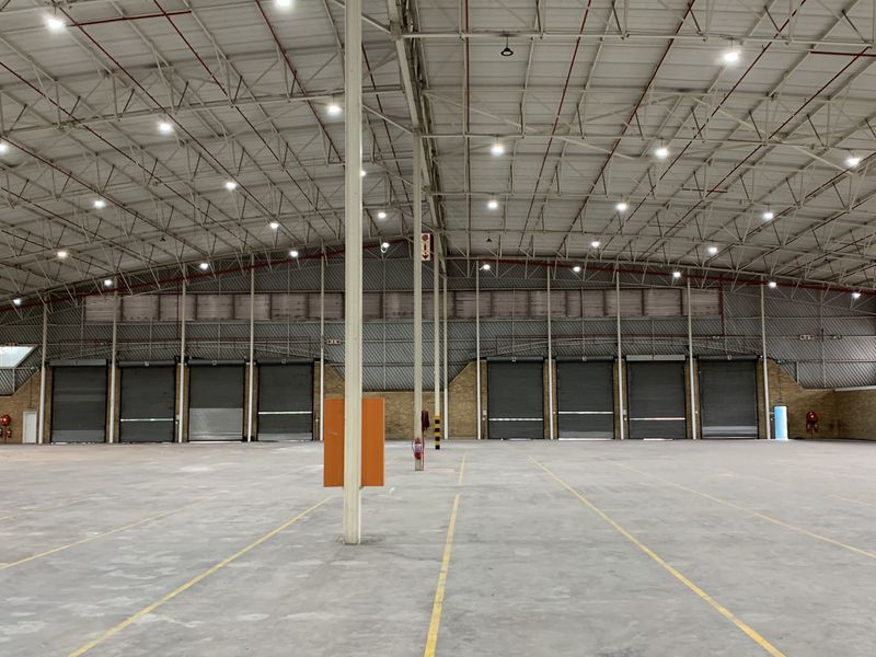 Spacious industrial warehouse featuring high ceilings, multiple roller shutter doors, concrete flooring, and integrated fire sprinkler system, suitable for logistics or manufacturing operations.