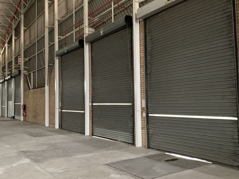 Spacious industrial warehouse interior featuring multiple roller shutter doors, high-clearance exposed steel truss roofing, and durable concrete flooring.