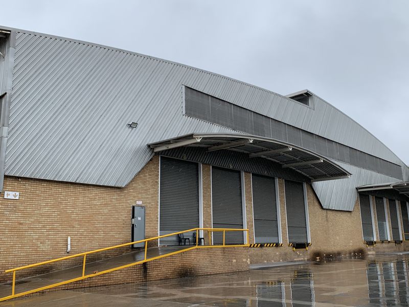 Industrial warehouse exterior featuring multiple roller shutter loading doors, a protective canopy, and a paved loading bay area.