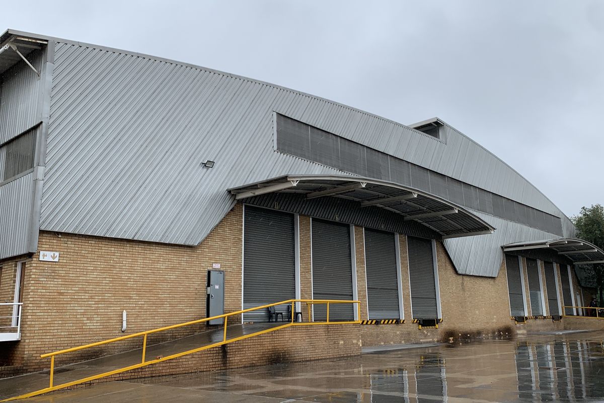 Industrial warehouse exterior featuring multiple roller shutter loading doors, a protective canopy, and a paved loading bay area.