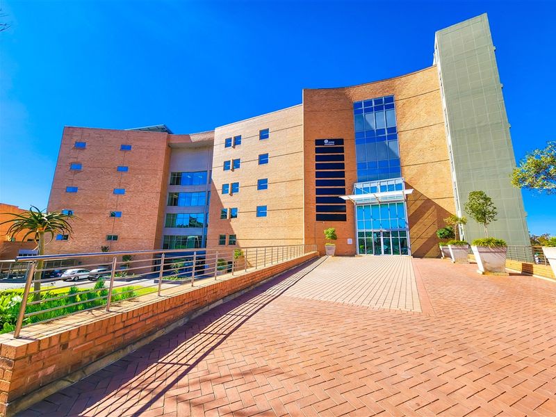 Modern multi-story office building featuring a prominent brick facade, glass curtain walling, and a spacious paved entrance plaza.